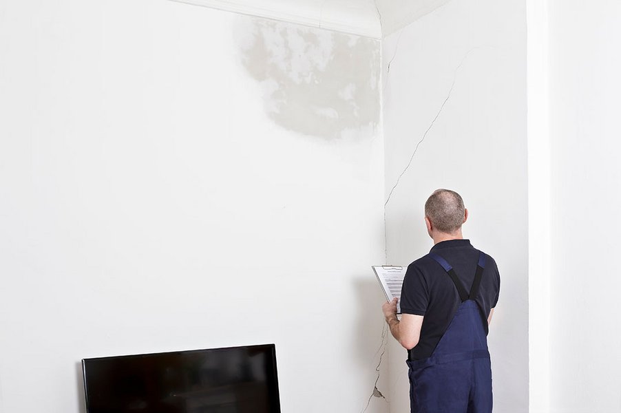 Ein Hausmeister kontrolliert als Teil der Haustechnik eine Wand, die nass ist und Risse hat